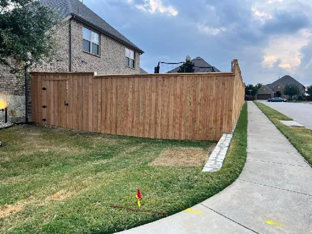 Wooden privacy fence enclosing a backyard, with grassy area and cloudy sky in the background.
